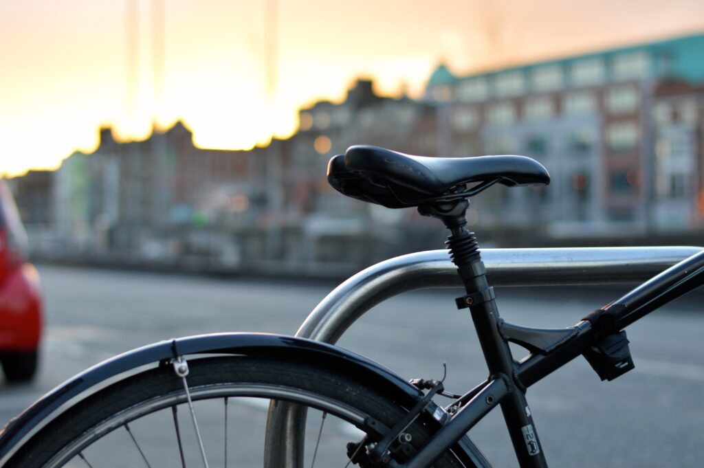 Bilden visar en cykel som står parkerad utomhus. Cykelställ vägg kan förenkla cykelhanteringen markant. Cykelparkering med ett fristående cykelställ skapar ordning i cykelrummet eller på cykelparkeringen.